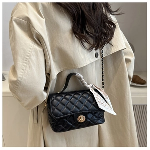 Quilted black leather crossbody bag with silk scarf handle detail worn over a beige coat