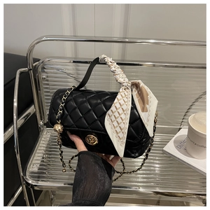 Detail of black quilted leather handbag with gold chain strap and silk scarf handle