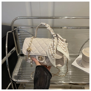Cream quilted leather handbag featuring a silk scarf handle and metal clasp on a bench