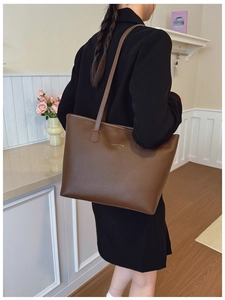 Detalle del bolso tote marrón oscuro en cuero mate con letras doradas y correas dobles