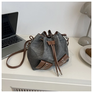Detail of retro denim bucket bag with brown leather trim and drawstring on a white desk
