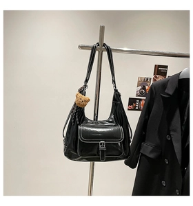 Detail of black semi-moon shoulder bag with white stitching and bear charm accessory