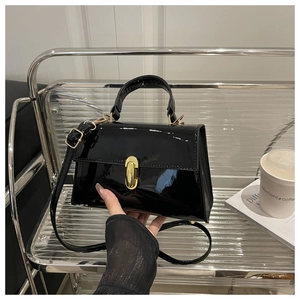 Detail of glossy black patent leather bag featuring a gold twist lock and top handle