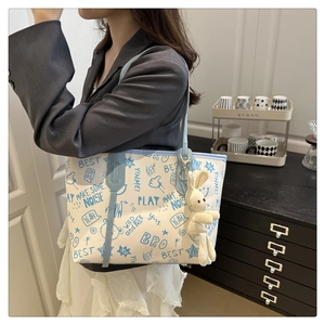 Détail d'un sac cabas blanc avec imprimé graffiti bleu et un pendentif lapin en peluche