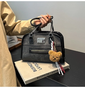 Detail of charcoal gray frosted faux leather Boston bag with plush bear charm and metallic accents