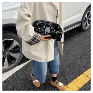 Détail de pochette en cuir verni plissé noir avec clous dorés dans un style urbain chic