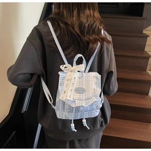 Detail of blue plaid school backpack with white lace trim and bow on wooden stairs
