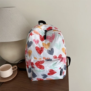 Sac à dos blanc avec imprimés cœurs colorés sur un bureau en bois avec lampe