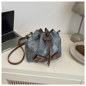 Detail of blue denim bucket bag with brown drawstrings on a white desk setup