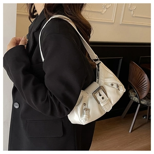 Detail of white pleated shoulder bag with large silver buckle and rivets on black suit