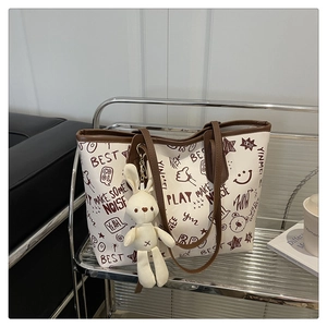 Détail d'un cabas blanc à graffitis avec bordure marron et pendentif lapin tricoté