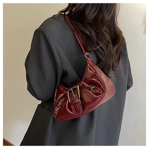 Detail of dark red patent leather shoulder bag with vintage buckles on grey blazer