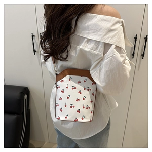 Detail shot of a white bucket bag with red cherry print and brown leather trim on a model