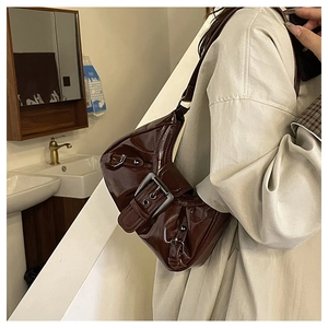 Close-up of dark brown patent leather shoulder bag with large silver buckles and studs