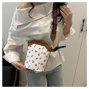Detail of white bucket bag with red cherry prints and geometric woven shoulder strap