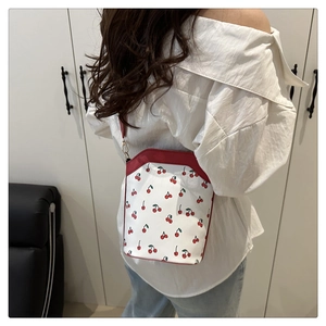 Detail of a cherry print bucket bag with red strap shown on model for size reference
