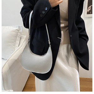 Model wearing a silver crescent underarm bag with litchi grain texture in a minimalist room