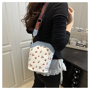 Detail of cherry print bucket bag featuring light blue trim and ethnic pattern strap