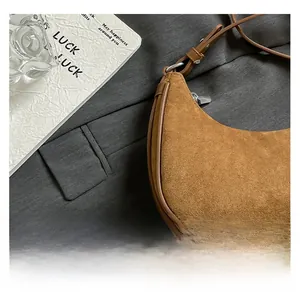 Close-up of brown suede crescent bag featuring smooth leather edges and metal zipper details