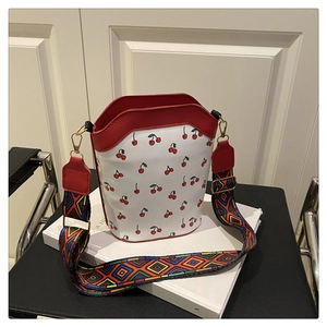 Detail of white cherry print bucket bag with red leather trim and woven strap