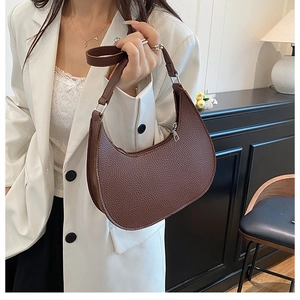 Close-up of deep brown lychee leather crescent bag on shoulder with silver zipper detail