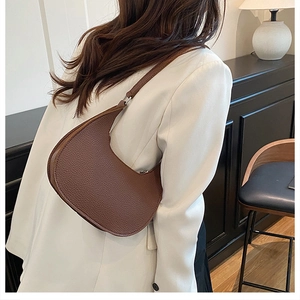 Detailed view of dark brown litchi grain leather crescent bag worn by a model in soft light