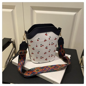 Detail of white cherry print bucket bag with colorful geometric woven shoulder strap