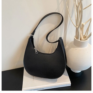 Detail of black crescent shoulder bag with lychee texture and silver zipper on white books
