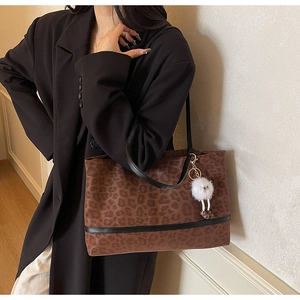Detail of leopard print tote bag with plush charm and black leather strap on shoulder