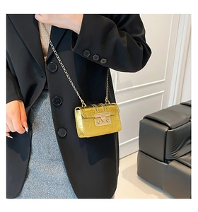 Dettaglio mini borsa dorata con catena e trama a coccodrillo su blazer nero