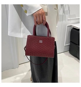 Detail of burgundy woven leather handbag with silver logo held by a person in a white suit