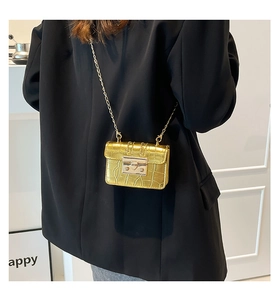 Detail of gold crocodile texture crossbody bag with metal chain strap on model