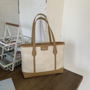 Large cream tote bag with brown leather trim on a wooden table in a minimalist setting
