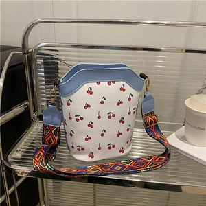 White cherry print bucket bag with colorful ethnic strap on a minimalist shelf