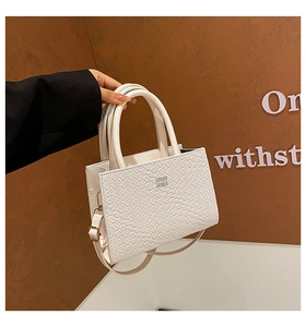 Detailed view of white woven leather texture and metallic logo on the stylish handbag
