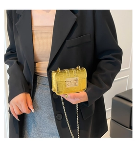 Close-up of a mini gold crocodile pattern chain bag held by a model in a suit