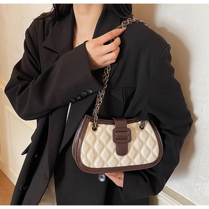 Detail of a beige quilted crossbody bag with brown trim and gold chain on model