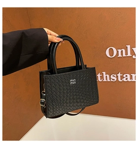 Detail of black woven texture handbag with round handles and metal logo held by model