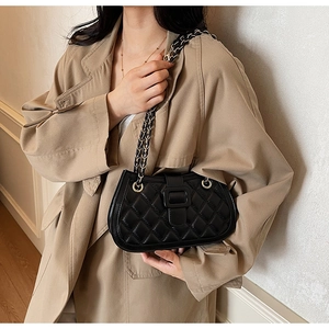 Close-up of black quilted leather shoulder bag with chain strap on a beige trench coat