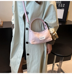 Sac à bandoulière en toile rose avec étiquette et charm ours porté sur un trench-coat léger