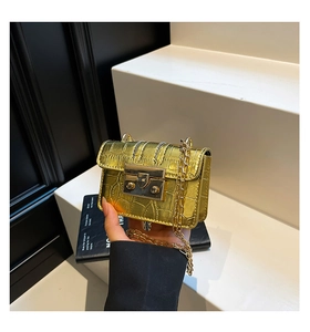 Close-up of golden croc-embossed square bag with metal chain strap and luxury buckle