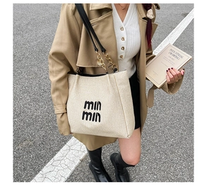 Detail view of beige woven tote bag with black embroidery and gold chain shoulder straps