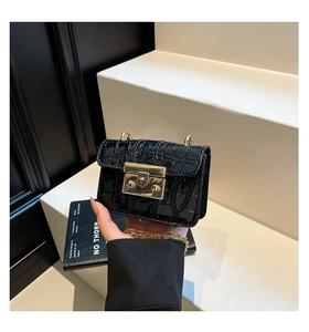 Detail shot of black crocodile pattern patent leather handbag with gold chain strap