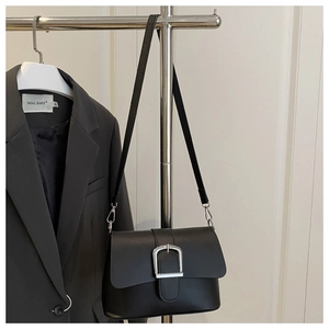 Detail of a black matte leather crossbody bag with a large silver buckle on a gray blazer