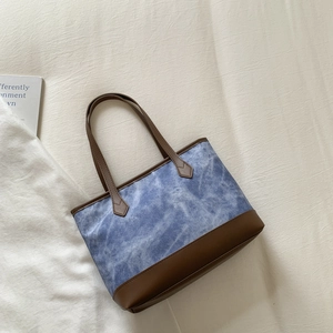 Detail of blue denim tote bag with brown leather stitching and trapezoid shape design