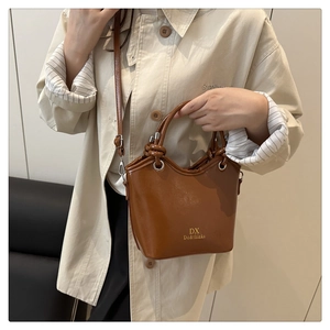 Detail of a brown glossy leather bucket bag with silver hardware on a beige coat