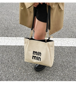 Detail of beige woven tote bag featuring black lettering and golden chain strap