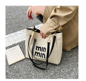 Detail of beige woven tote bag featuring min min lettering and black chain handles