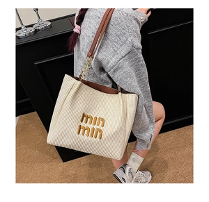 Detailed macro view of woven beige tote bag featuring gold embroidery and leather chain handles