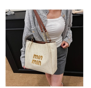 Detail of cream woven tote bag with brown embroidery and leather chain strap on model